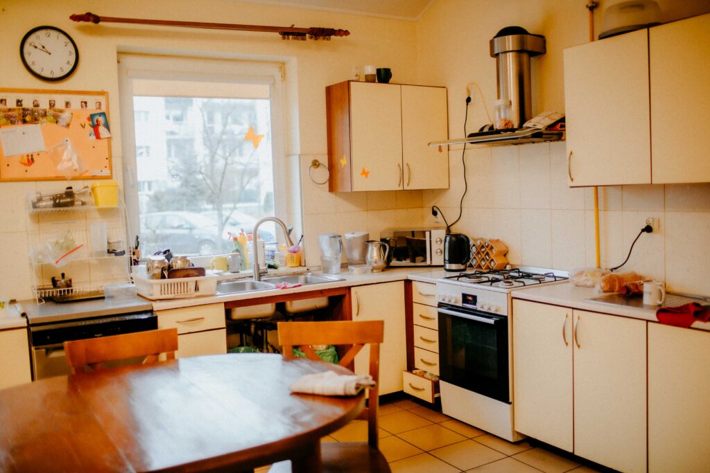Pomieszczenie kuchenne. W kuchni znajduje się stół z krzesłami, szafki kuchenne, piekarnik, zmywarka. Kuchnia jest wyposażona w sprzęty: czajnik do wody, mikrofalówkę, dzbanki, suszarkę.